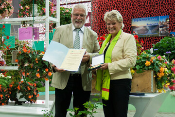  Zweifacher Erfolg fr die Aufbaugemeinschaft (AFG) des Landesverbands Gartenbau im Saarland e.V.. Gnther Hoffmann-Schuster (li.), Prsident des Landesverbands Gartenbau im Saarland e.V., nimmt stellvertretend fr die AFG die Auszeichnungen von DBG-Ausstellungsbeauftragten Renate Behrmann (re.) entgegen. Fr eine beispielhafte Prsentation von Gemse und Krutern in Kombination mit blhenden Pflanzen erhlt die AFG den Ehrenpreis der Landwirtschaftskammer fr das Saarland; die Groe Goldmedaille der DBG gewinnt sie fr eine harmonische Gestaltung einer groen Pflanzensorten- und Artenvielfalt sowie eine ausdrucksstarke Umsetzung des Grundkonzeptes der Blumenhalle. Foto: DBG