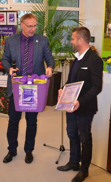 Auszeichnung von Jannik Hoffmann und seinem Team von Blumenhaus Chrysanthem als bester Vertragsbetrieb 2018. Stefan Friedel, links, Geschftsfhrer der Treuhandstelle fr Dauergrabpflege Hessen Thringen, bergibt einen lila Korb mit Prsenten fr das gesamte Team. 